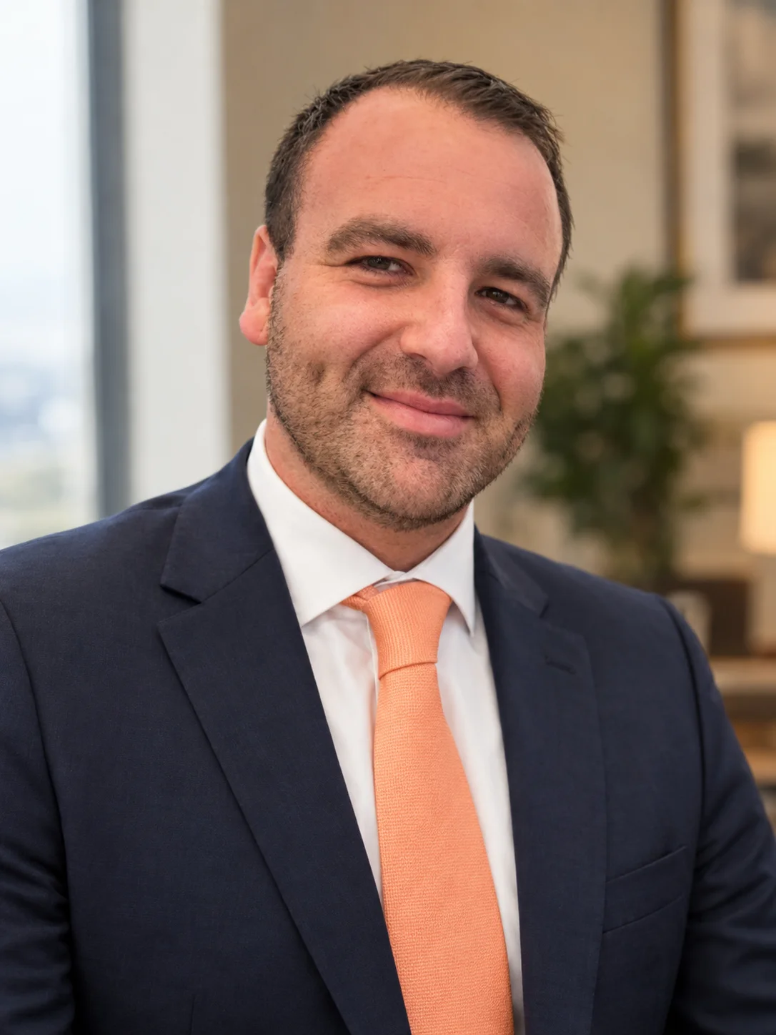 Ryan Mifsud of Orange Lease, smiling, in a navy suit and orange tie